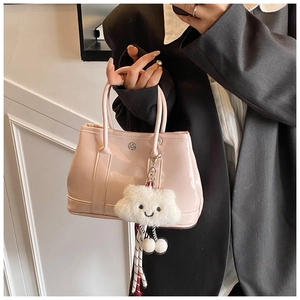 Pink patent leather handbag with a plush cloud charm held by a model in a black suit