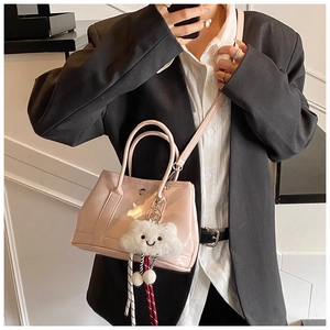 Close-up of light pink glossy handbag with plush cloud charm on a business suit