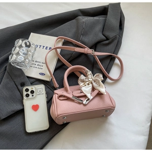 Detail einer rosa Lederhandtasche mit Seidenschleife auf einer grauen Anzugjacke