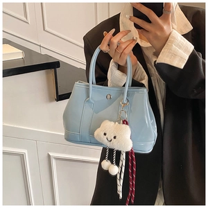 Close-up of light blue glossy bucket bag featuring a plush cloud charm and patent texture
