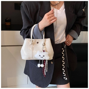 Close-up of beige glossy bucket bag with plush cloud charm styled on black blazer
