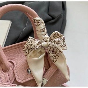 Detailansicht einer rosa Lederhandtasche mit dekorativem Seidentuch am Tragegriff