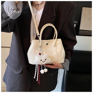 Detail of cream bucket bag with metal buckle and plush cloud charm on a shoulder strap