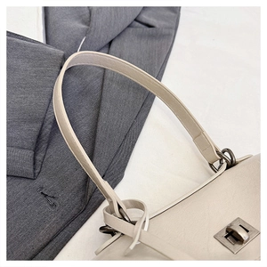 Macro detail of beige leather stitching and vintage metal twist lock on shoulder bag