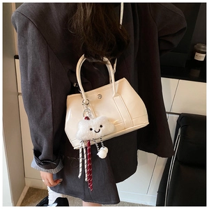 Detail of beige patent leather bucket bag with plush cloud charm and crossbody strap