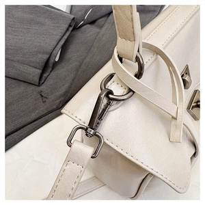 Detailed macro view of matte gunmetal hardware and litchi texture on beige handbag