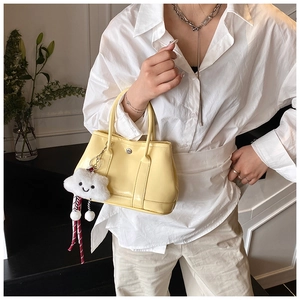 Detail of pale yellow glossy bucket bag featuring a plush white cloud smiley charm