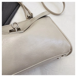 Detail of metal twist lock and fine stitching on the cream leather handbag base