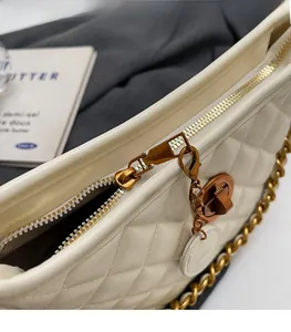 Close-up of white quilted bucket bag featuring a gold metal zipper and chain strap