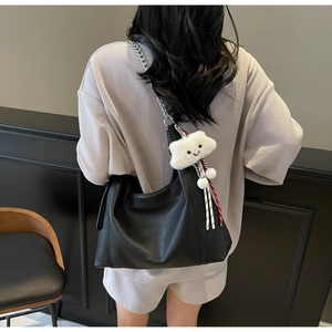 Detail of black pebbled leather hobo bag with silver chain and plush charm