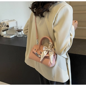 Rosafarbene Handtasche aus Leder mit dekorativem Seidenschal am Model im Café