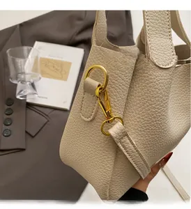 Macro detail of lychee grain leather and gold hardware on beige bucket bag