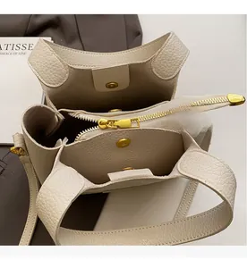 Detail of cream bucket bag showing smooth gold zipper, magnetic snap, and inner pockets
