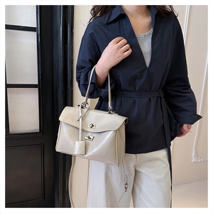 Detail of beige glossy leather handbag featuring dual twist locks and adjustable strap