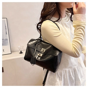 Close-up of black retro leather shoulder bag with dual gold twist-lock buckles on the flap