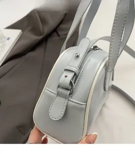 Detail of adjustable strap and white piping on a light blue faux leather semi-round bag