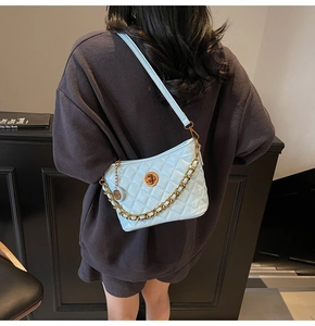 Detail of light blue quilted leather bag with gold chain strap on a model shoulder