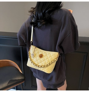 Detail of light yellow quilted bucket bag with gold chain strap on a model shoulder