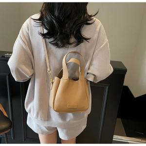 Detail of light brown lychee grain leather bucket bag with top handles and logo plate