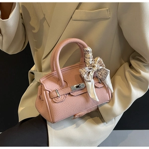 Detail einer rosa Handtasche aus Leder mit Seidenschal und Metall-Drehverschluss