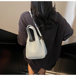 Detail of light gray bucket bag showing lychee leather texture and golden metal hardware