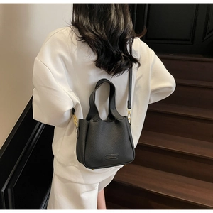 Detail of black lychee grain leather bucket bag with metallic logo and adjustable strap