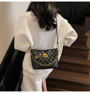 Detail of black quilted crossbody bag with gold chain and circular turn-lock closure