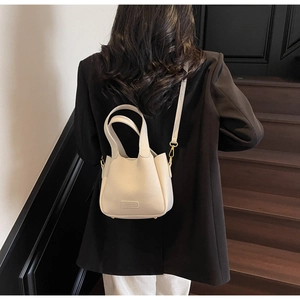 Crossbody shot of a creamy white lychee grain bucket bag with gold hardware detail