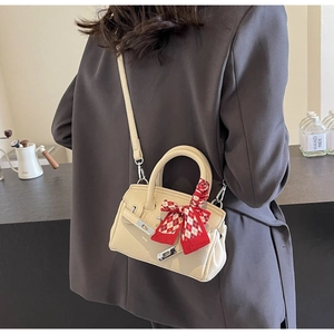 Detail der beige Handtasche aus Leder mit rot-weißem Seidenschal am runden Griff