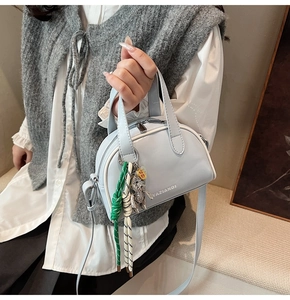 Detail of blue crossbody bag with white piping and metallic bear charm accessory