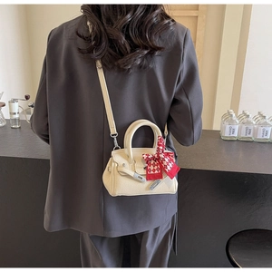 Detail einer beigen Lederhandtasche mit rotem Seidenschal am Griff und Lychee-Muster