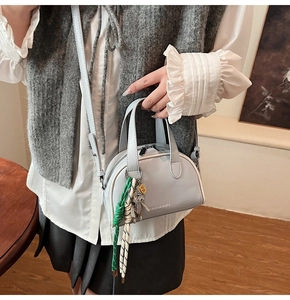 Close-up of a light grey crossbody bag with silver doll charm and YAZIANDI logo