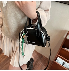 Detail view of black glossy handbag with white trim, silver bear charm and logo