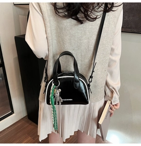 Detail view of black glossy half-round crossbody bag with white piping and bear charm