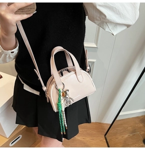 Detail of a light pink mini crossbody bag with metal bear charm and woven keychain