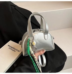 Close-up of metallic silver bag with bear charm and green braided rope detail