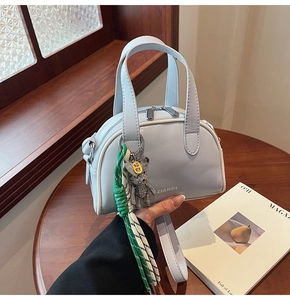 Grey matte leather mini Boston bag with bear charm and woven rope on a wooden table