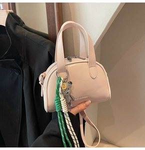 Detail of light pink mini satchel featuring double zippers and cute bear charm