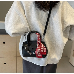 Detail einer schwarzen Mini-Handtasche aus genarbtem Leder mit Seidenschal am Handgriff