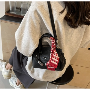 Detail einer schwarzen Mini-Handtasche aus Leder mit kariertem Seidentuch am Griff