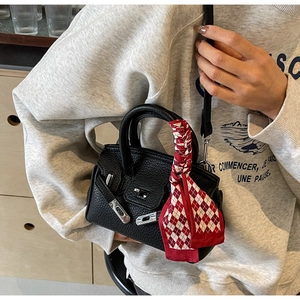 Detail einer schwarzen Lederhandtasche mit Narbenstruktur, Silberverschluss und Seidenschal