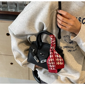 Detail einer schwarzen Mini-Handtasche mit Lederkörnung und Seidenschal am oberen Griff