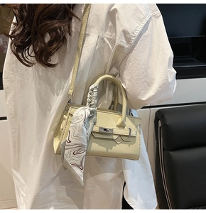 Detail der eleganten beigen Leder-Quadrattasche mit dekorativem Seidenschal am Tragegriff