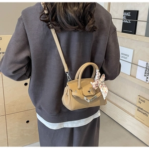 Detailansicht der khakifarbenen Mini-Handtasche mit Seidenschal-Griff auf Holzregal