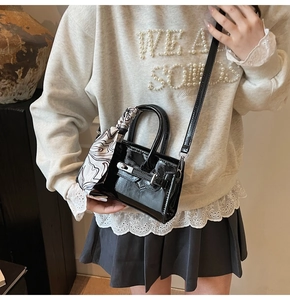 Detail einer glänzenden schwarzen Mini-Handtasche mit Seidenschal-Griff und Drehverschluss