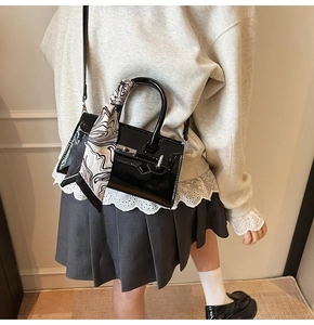 Details einer schwarzen Lackleder-Handtasche mit Seidentuch am Griff und Metallverschluss