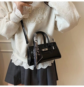 Detail einer glänzenden schwarzen Lackledertasche mit silbernem Drehverschluss und Seidenschal