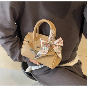 Detailaufnahme einer beigefarbenen Lederhandtasche mit gebundenem Seidentuch am Tragegriff