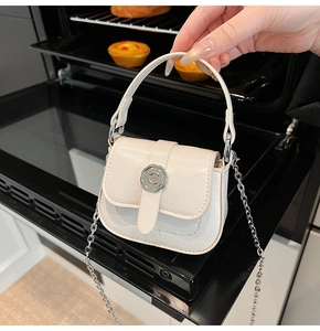 Detail of cream mini square bag showing shiny texture, silver C buckle, and chain strap