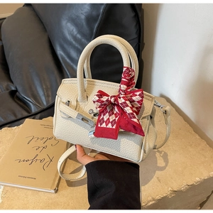 Nahaufnahme der cremefarbenen Ledertasche mit silberner Schließe und Seidenschal-Griff